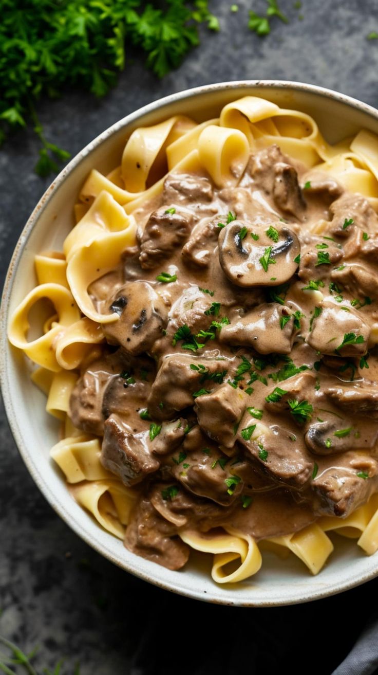 a white bowl filled with pasta covered in mushroom sauce and garnished with parsley