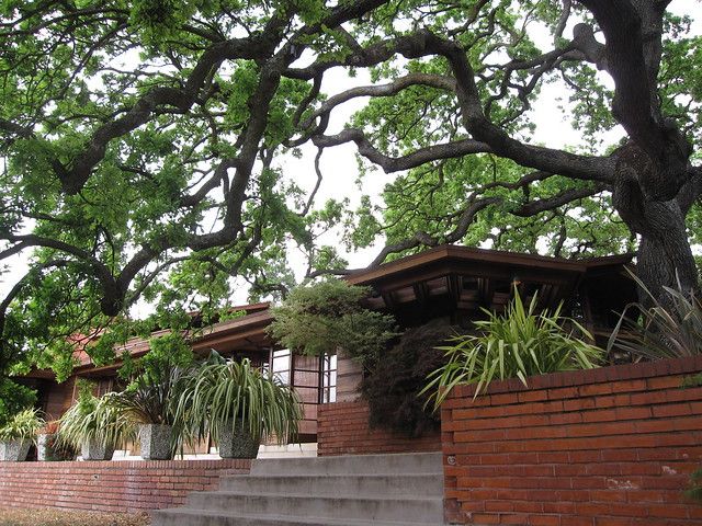 a brick house with stairs leading up to it and trees in the front yard area