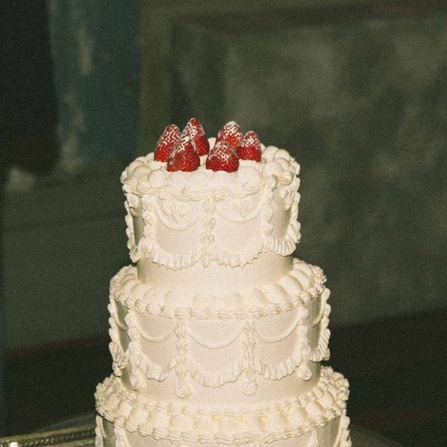 a three tiered white cake with strawberries on top is sitting on a silver platter