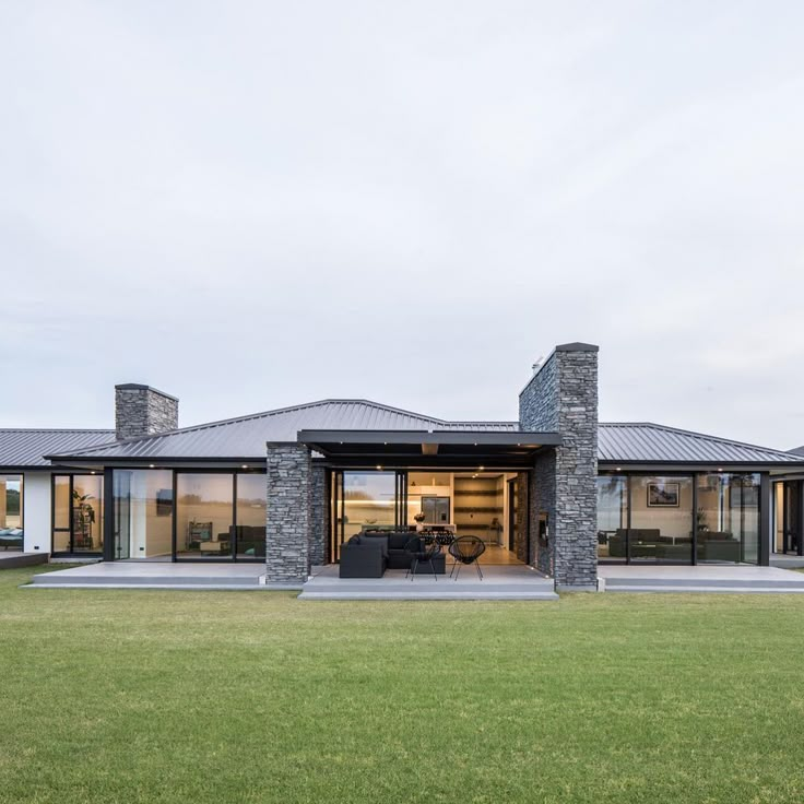 a modern house with glass walls and stone pillars on the front lawn, surrounded by lush green grass