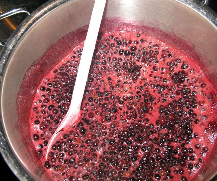 a metal bowl filled with red liquid and blackberries next to a white plastic spoon