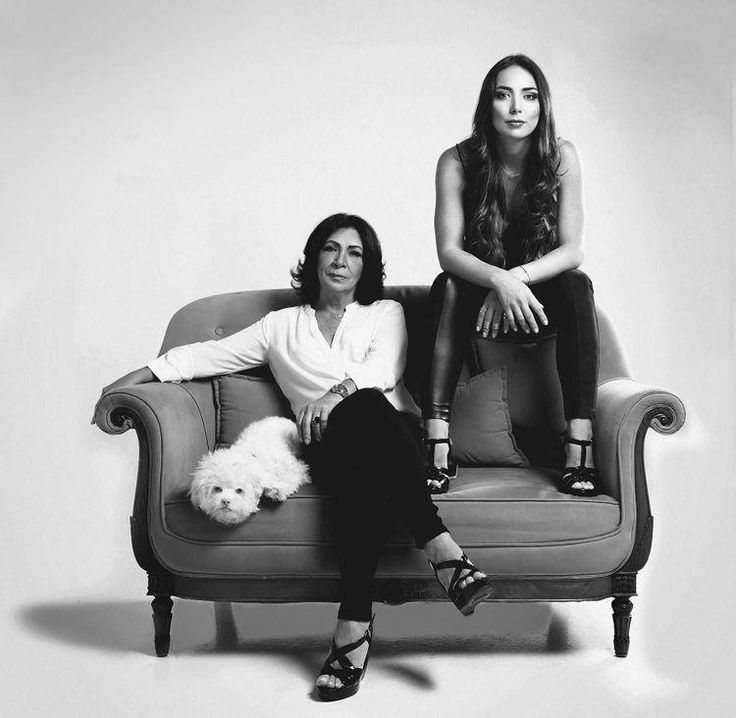 two women sitting on top of a couch with a white dog in front of them