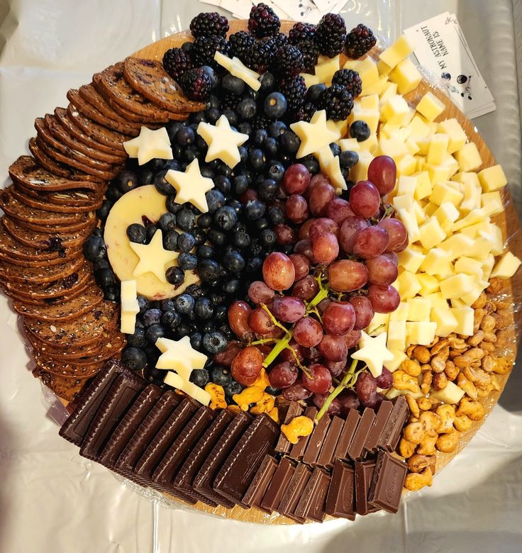 a platter filled with crackers, grapes, nuts and cheeses on top of a white table cloth