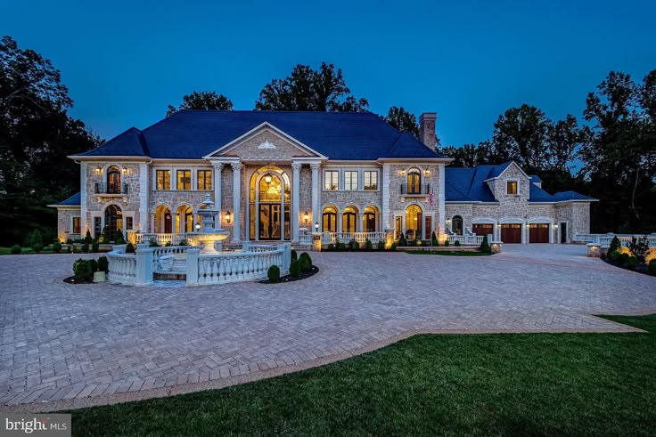 a large house with a fountain in the front yard at night time, surrounded by trees and bushes