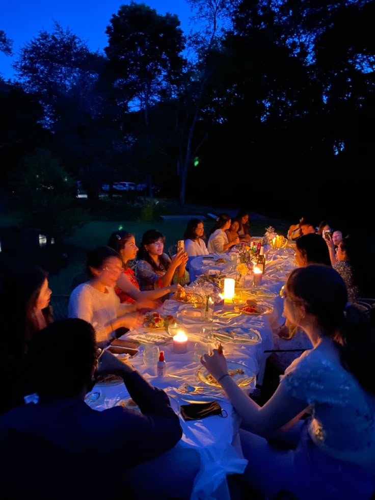 a group of people sitting around a table with candles in their hands at night time