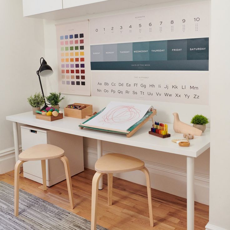 a white desk with two stools and a calendar on the wall behind it,