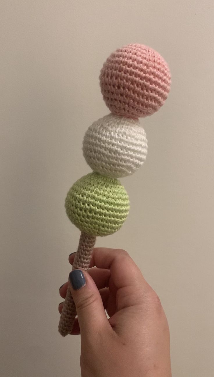 a hand holding a crocheted toy with three balls on it's top