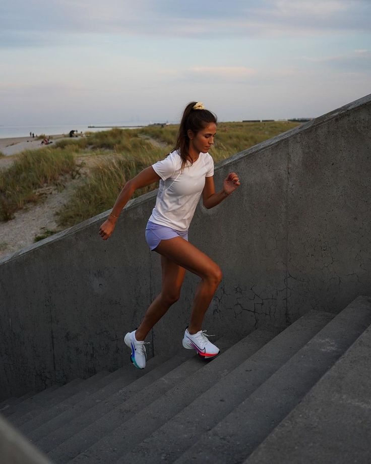 a woman is running down some stairs by the beach