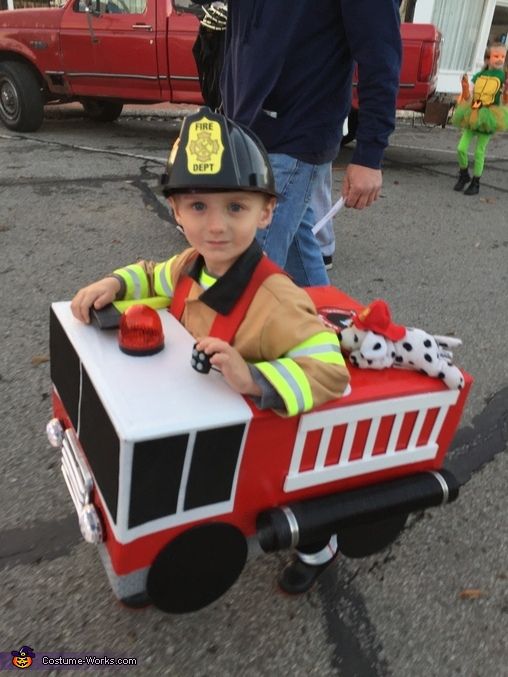 a young boy dressed as a fireman riding on top of a small train car