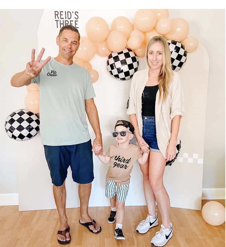 a man, woman and child standing in front of a backdrop with checkered balloons