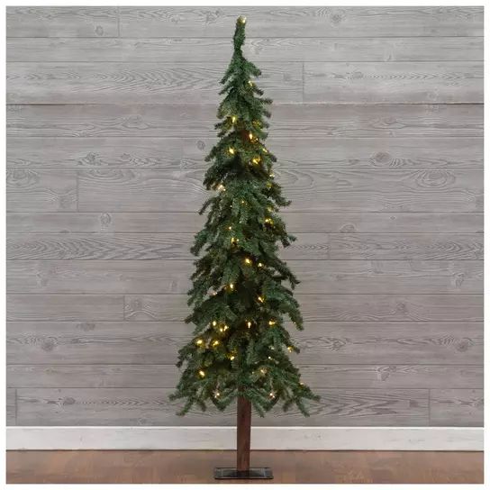 a small christmas tree with lights on it in front of a wooden wall and floor