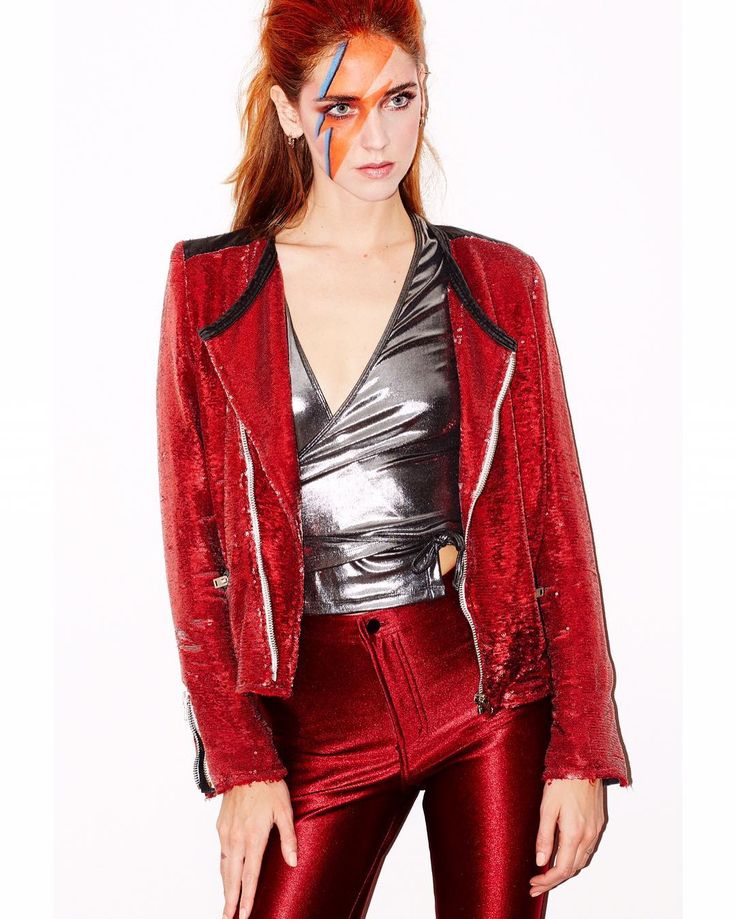 a woman with red hair and makeup is wearing a red jacket, silver top and metallic pants