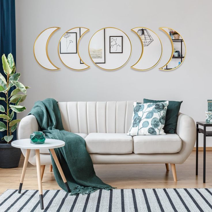 a living room with white couches and green throw pillows on the rug, surrounded by three circular mirrors