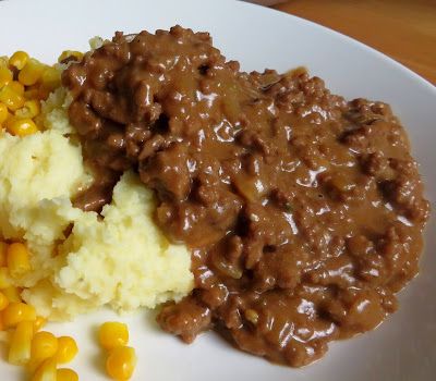 a white plate topped with mashed potatoes and gravy next to corn on the cob