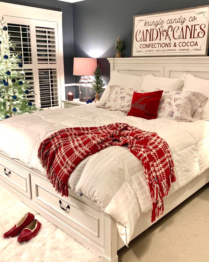 a white bed with red pillows and blankets on it in front of a christmas tree