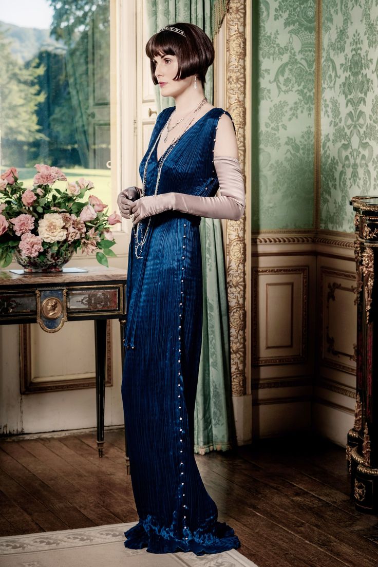 a woman standing in front of a window wearing a blue dress with pearls on it