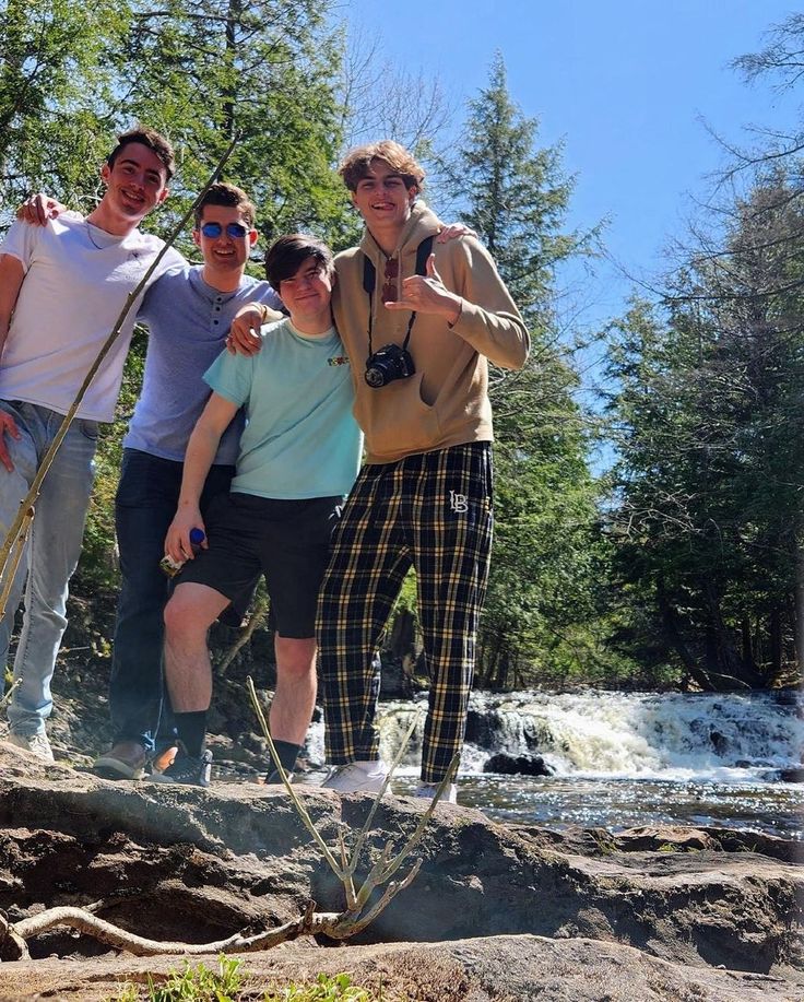 four people posing for a photo in front of a waterfall with trees and water behind them