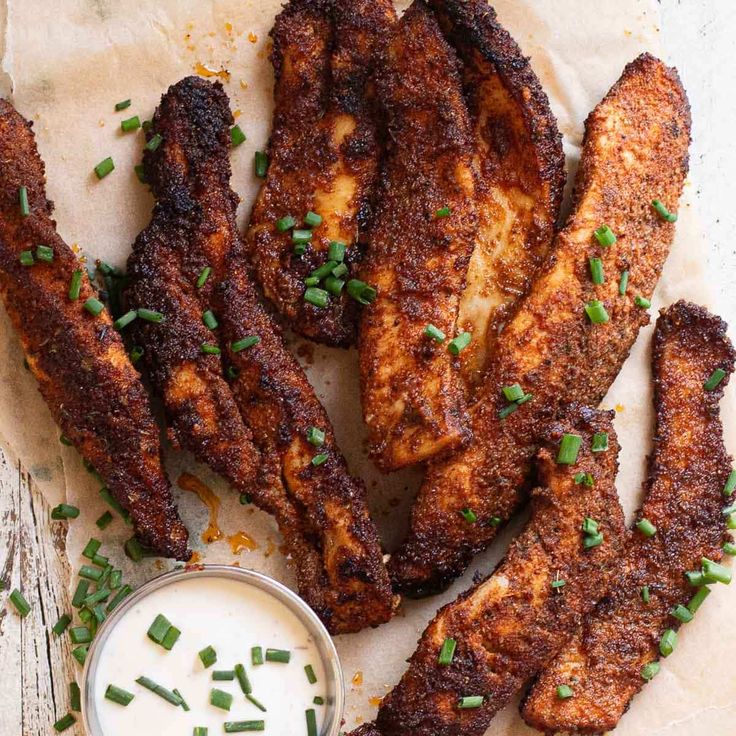 chicken wings with ranch sauce and chives on parchment paper next to small bowl of ranch dressing