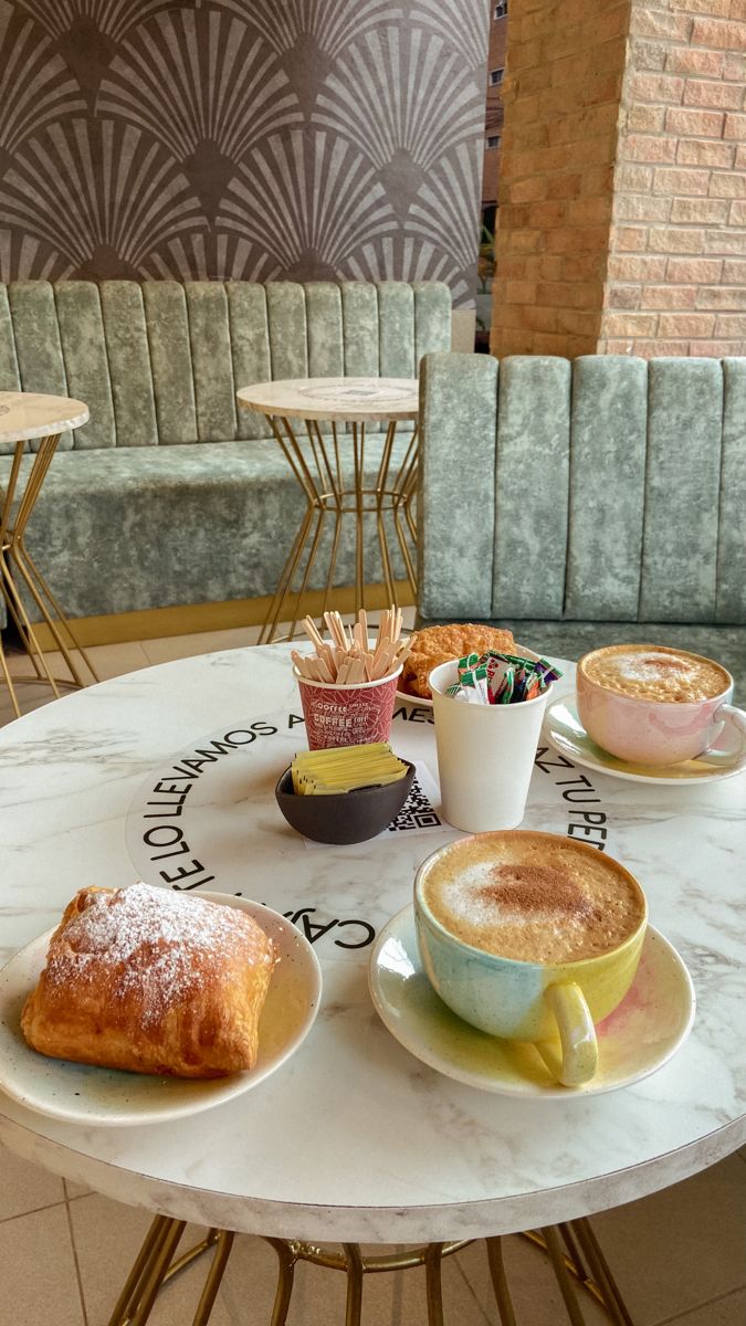 a table topped with two cups of coffee and pastries on top of plates next to each other