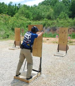 a man is practicing his shooting skills at the range in an open area with trees and bushes behind him