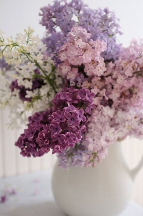 a white vase filled with lots of purple and white flowers