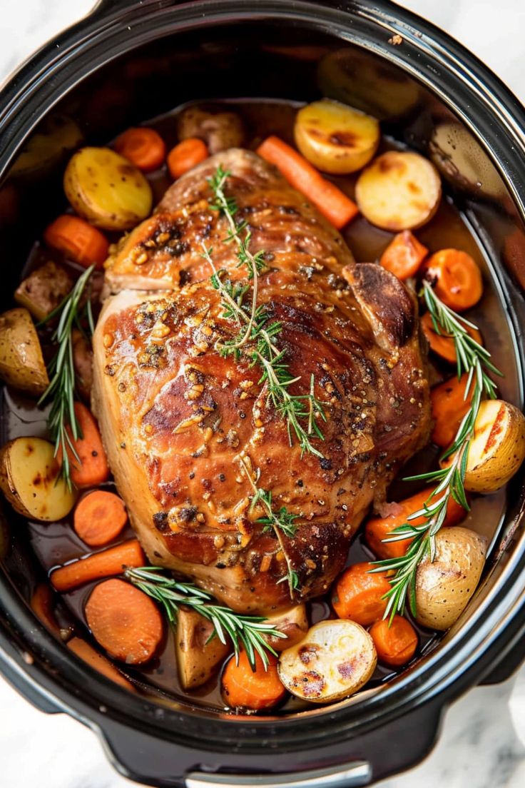 a pork roast in a slow cooker with carrots, potatoes and rosemary sprigs