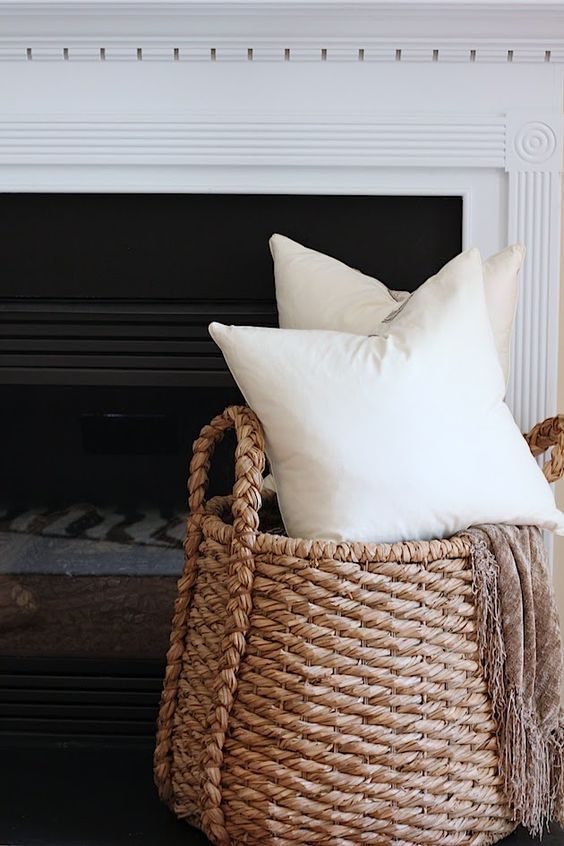 a basket filled with pillows next to a fire place