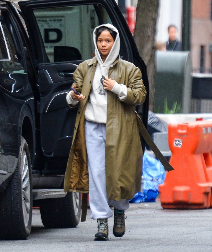 a woman is walking down the street with her cell phone in her hand and wearing a raincoat