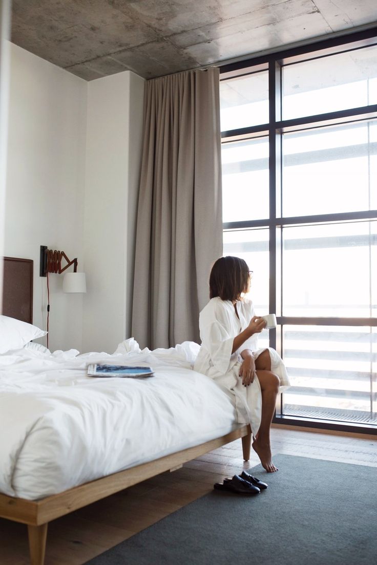 a woman sitting on top of a bed in a bedroom next to a large window