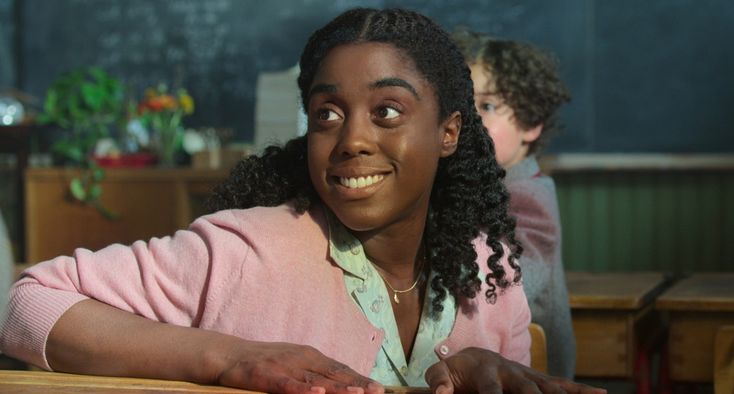 a young woman sitting at a desk with her hands on the table and looking up