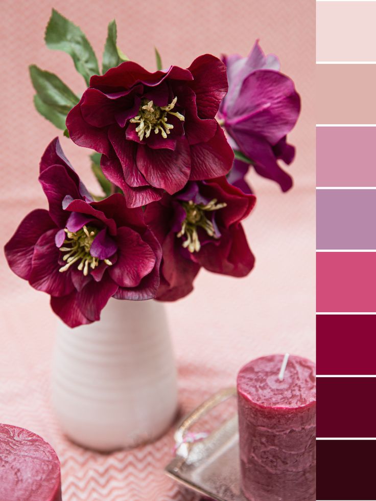 a white vase filled with purple flowers next to two candles and a pink table cloth