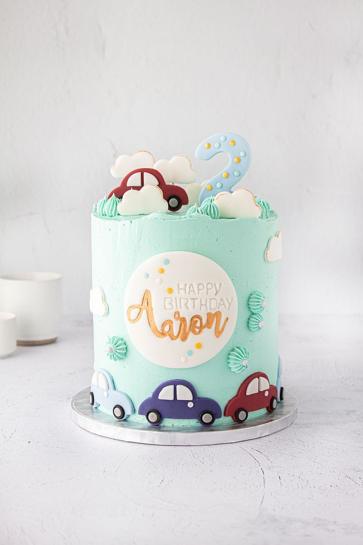 a birthday cake with cars and clouds on the top is decorated in pastel blue frosting