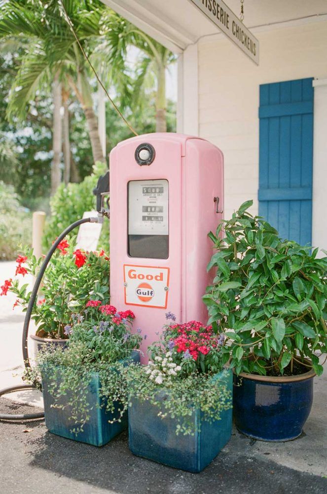 a pink gas pump sitting next to some potted plants