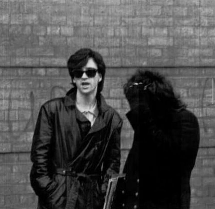 a man standing next to a woman in front of a brick wall with an animal on it