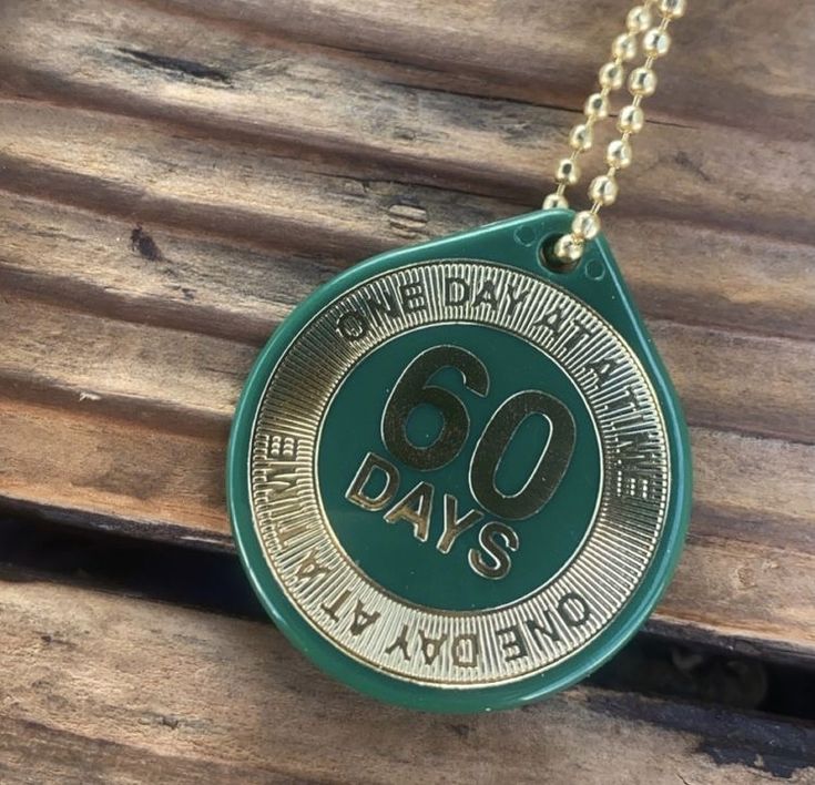 a green and gold necklace with the words 60 days on it hanging from a chain