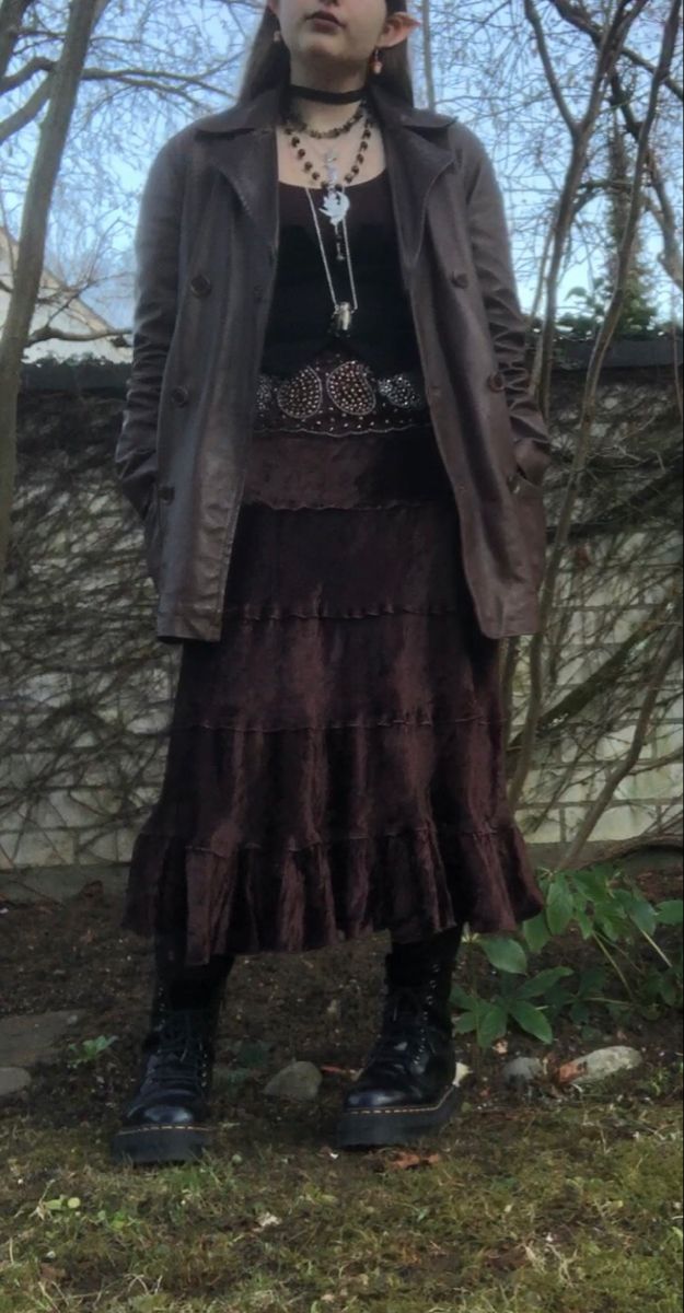 A mid-size person/girl wearing mate rose lipstik, a black tight waistcoat with a ripped stocking selfmade longsleeve and a thrifted dark brown maxi skirt, black dr. Martins and multiple crystal rings and bracelets. 	The person is also wearing multiple silver necklaces, one in form of a dragonfly and another in form of a moon, a green crystal bead necklace and a black lace choker. Dark Witchy Outfits Aesthetic, Dark Forest Outfit Aesthetic, Dark Forest Core Outfit, Dark Fairycore Costume, Woodland Goth Aesthetic Outfits, Autumn Fairycore Outfits, Cottage Goth Aesthetic Outfits, Moss Core Aesthetic Outfits, Cottage Punk Fashion