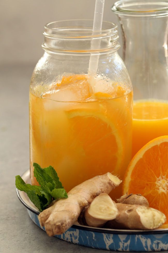 orange juice in a glass jar next to sliced oranges and ginger on a plate