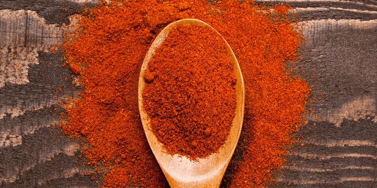 a wooden spoon filled with red powder on top of a wooden table next to an orange substance