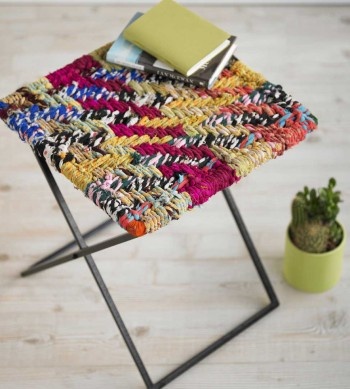 a multicolored rug sitting on top of a metal stool next to a potted plant