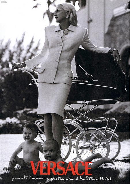 a woman is standing next to a baby in a stroller and another child sits on the ground