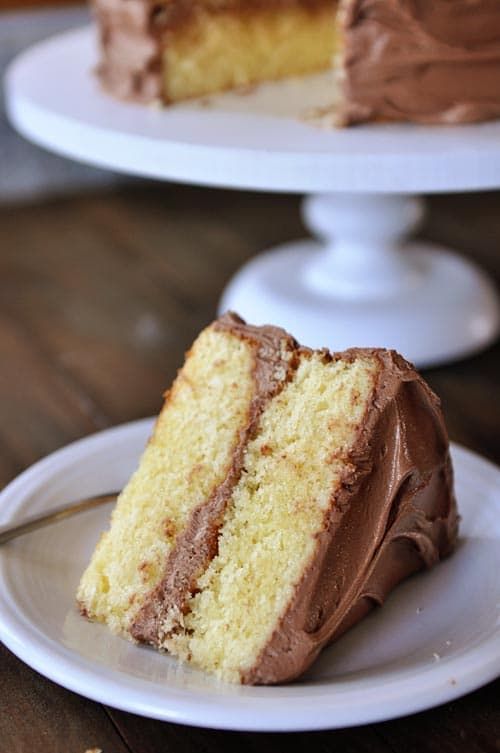 a slice of cake with chocolate frosting on a plate next to the rest of the cake