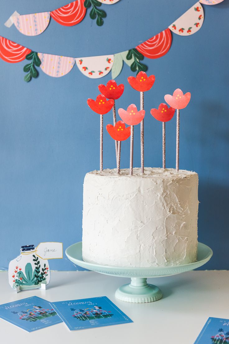 a white cake topped with lots of red flowers on top of a table next to cards