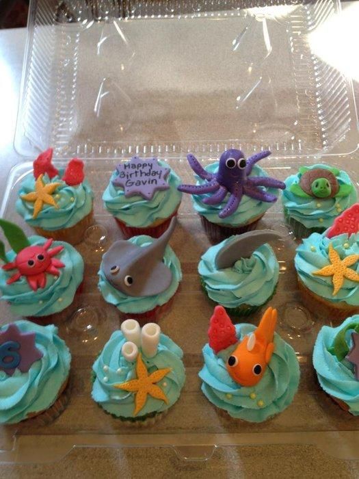 cupcakes with blue frosting and sea creatures on them sitting in a plastic tray