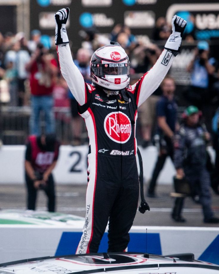 a man standing on top of a race car raising his hands in the air and celebrating