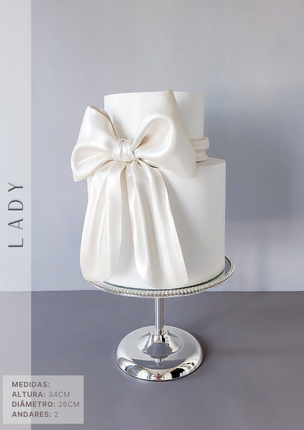 a white wedding cake with a large bow on it's top is displayed in front of a gray background