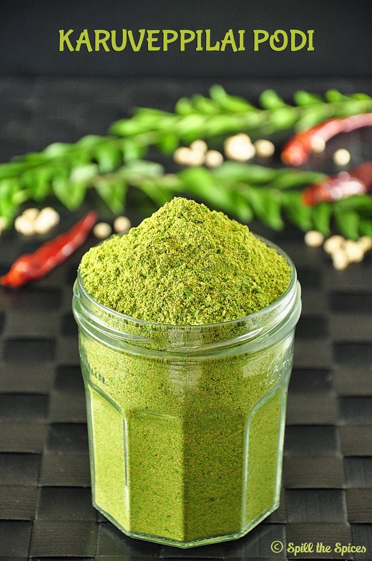 a jar filled with green powder sitting on top of a black table next to chili peppers