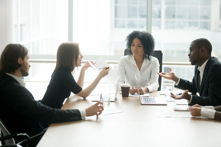 a group of people sitting around a table talking to each other in a meeting room