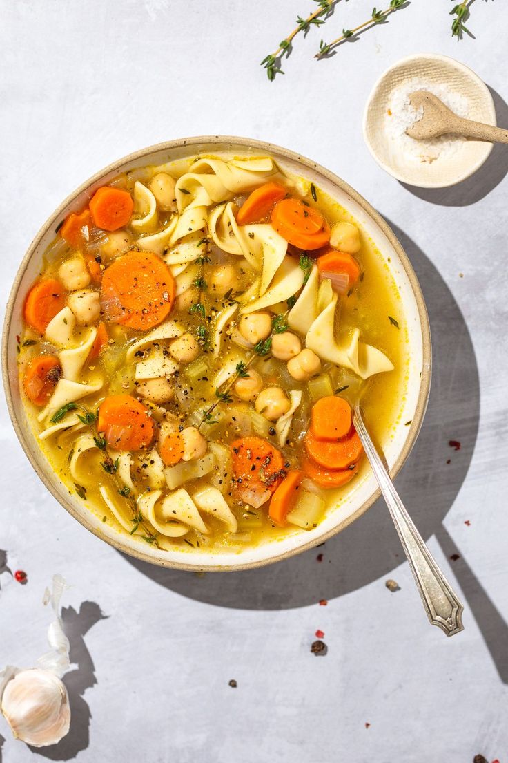 a bowl of pasta soup with carrots and parsley on the side next to a spoon