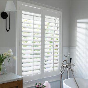 a white bath tub sitting in a bathroom next to a window with shutters on it