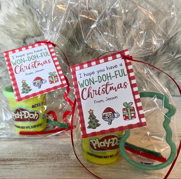 two christmas gift bags sitting on top of a wooden table next to a plastic bag